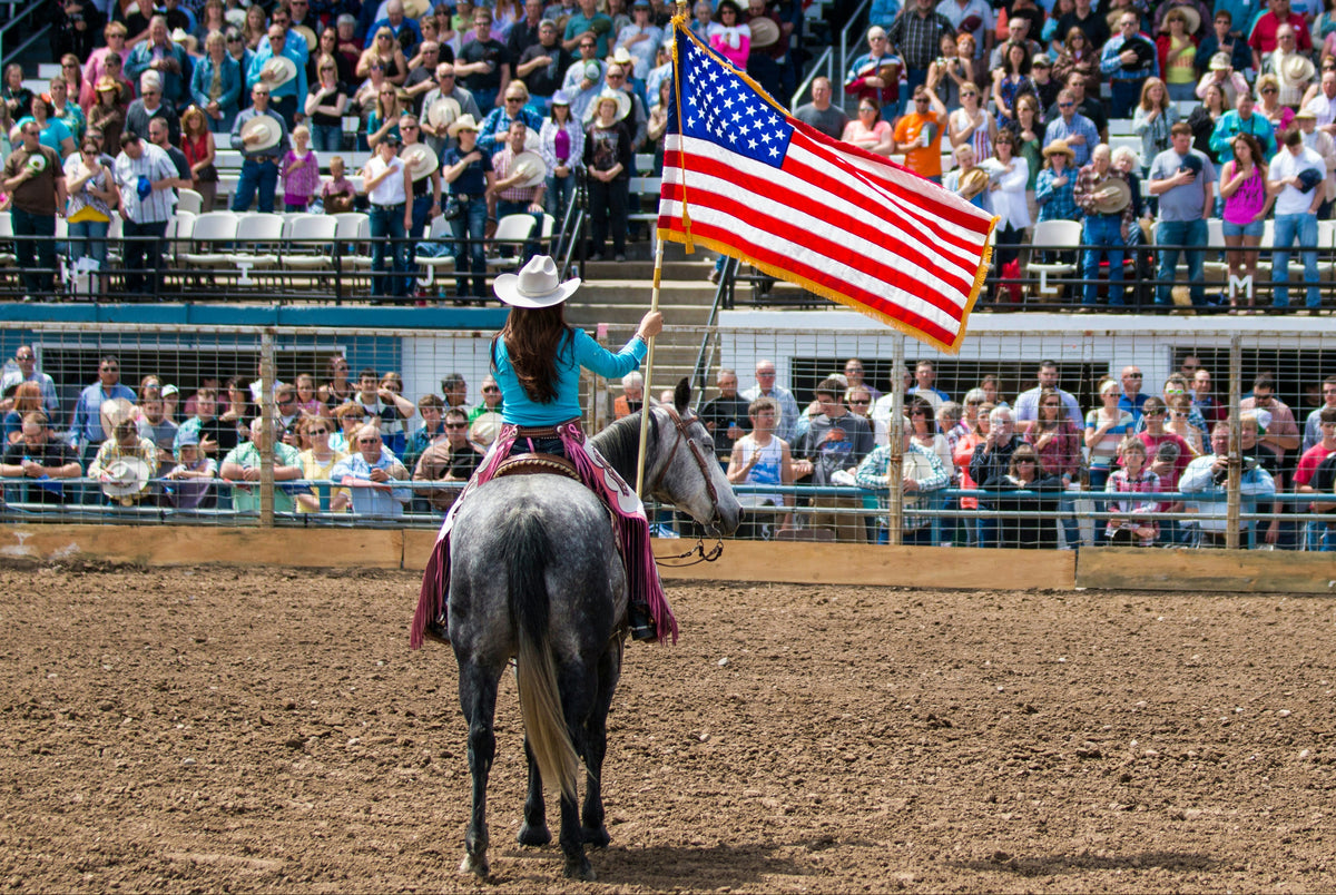Person on horseback holding an American flag in front of a crowd at a rodeo event 